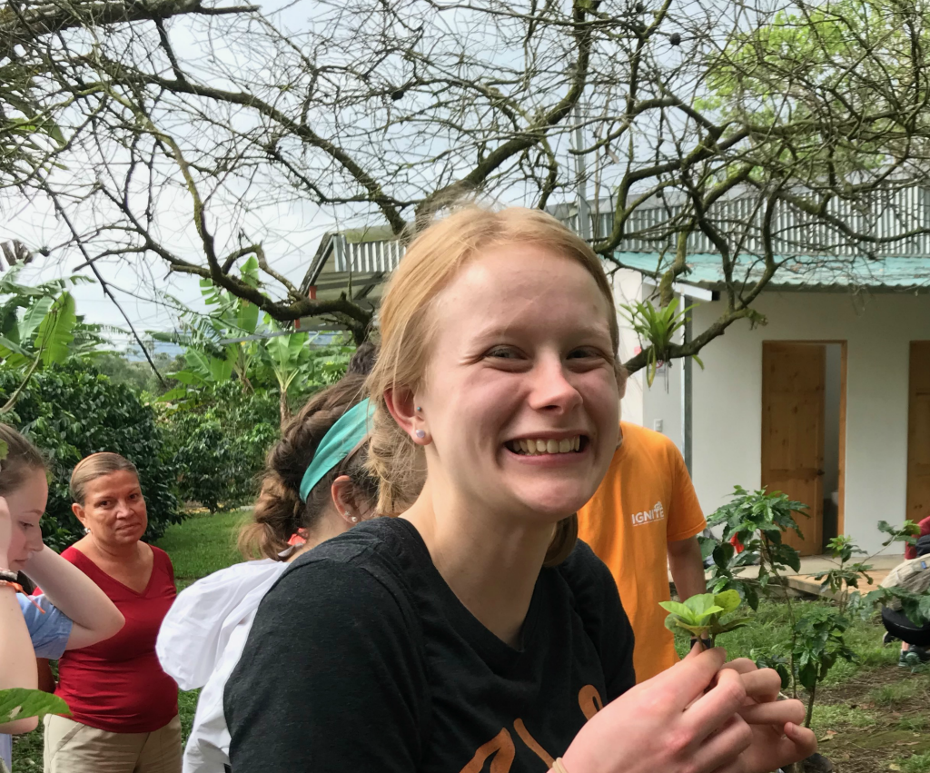 A female student holds a small plant and smiles as greens are harvested on a study abroad trip to Costa Rica.