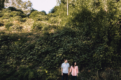 A male and female couple hold hands in front of a bank covered in kudzu vine