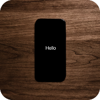black cell phone laying on a wood surface with the word hello in white modern font on the screen of the phone