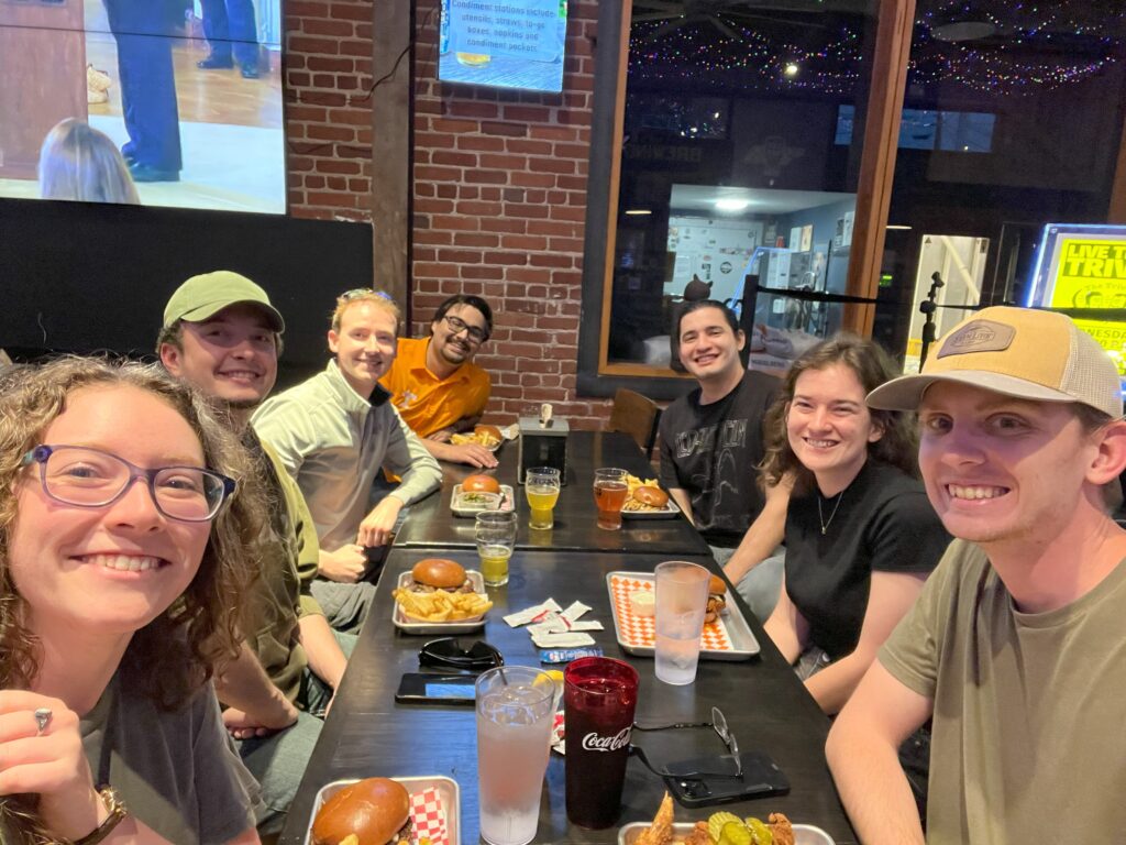 A group of students looking at the camera smiling while sharing food and drink at a restaurant