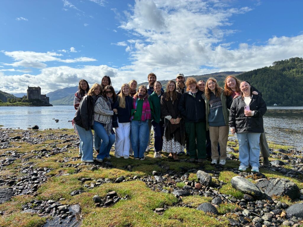 Students in a group smiling with water behind them