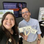 Woman and man smiling at the camera holding up fake money