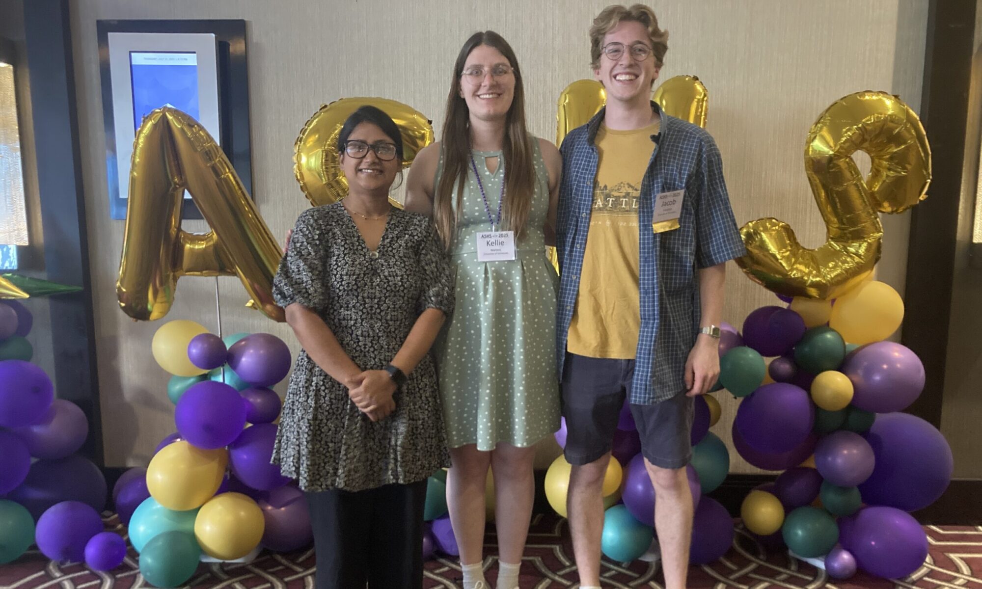 Photo of three people smiling in front of balloons