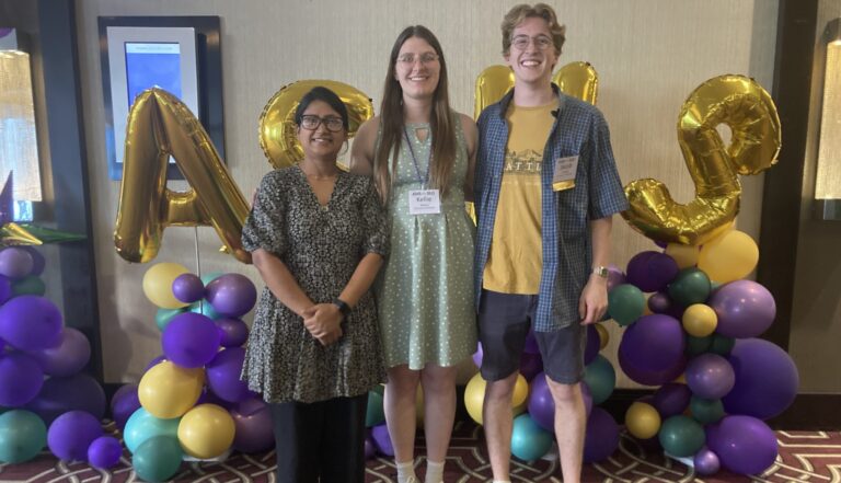 Photo of three people smiling in front of balloons
