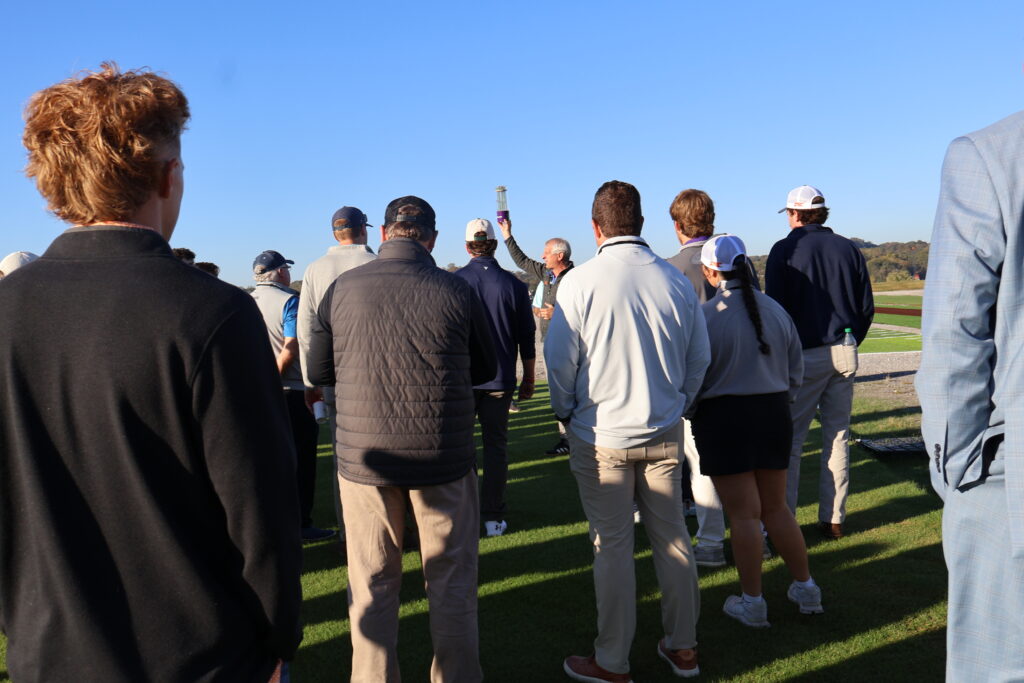 Man raising a tube with grass in it and showing it to a large group
