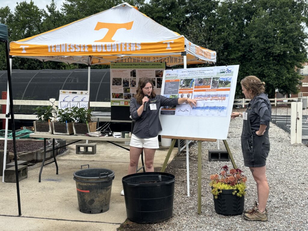 Two women presenting a research poster outside near a tent