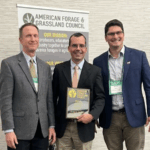 Three men smiling with the man in the middle holding an award