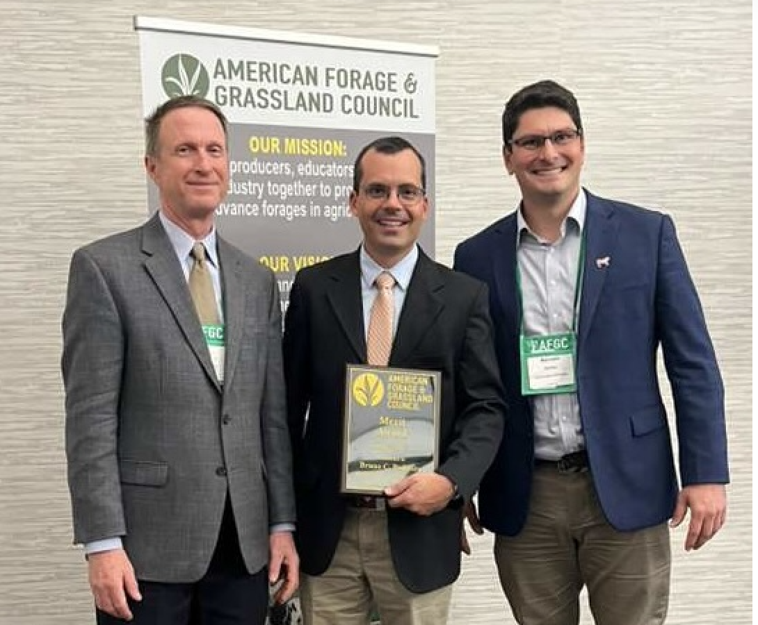 Three men smiling with the man in the middle holding an award