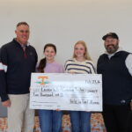 Two men and two women smiling at the camera holding a large check