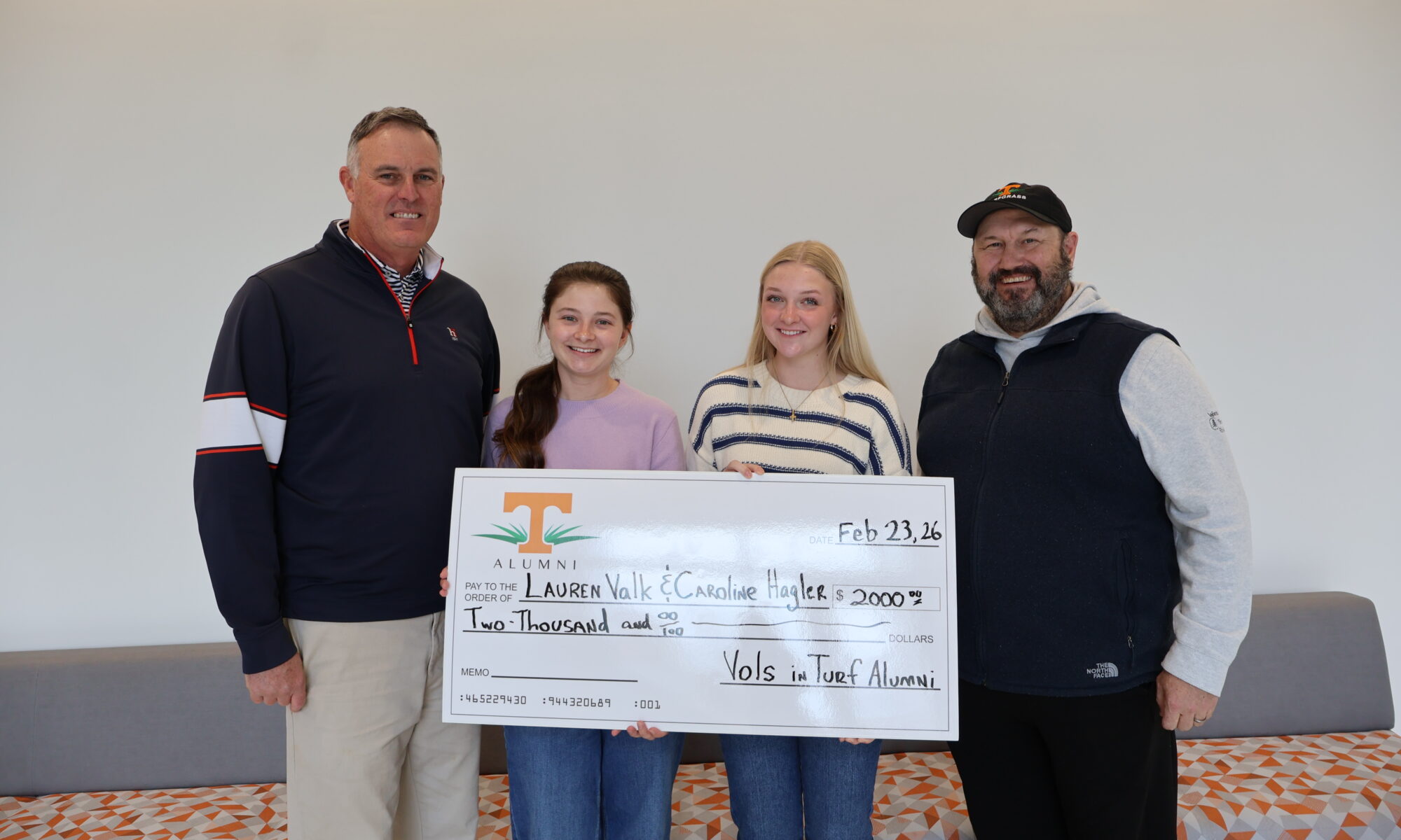 Two men and two women smiling at the camera holding a large check