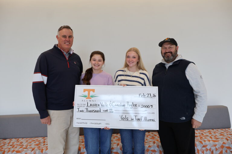 Two men and two women smiling at the camera holding a large check