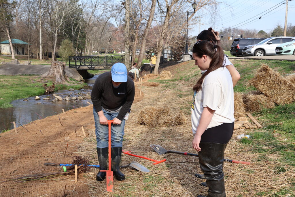 Two people watching someone making a hole in the ground