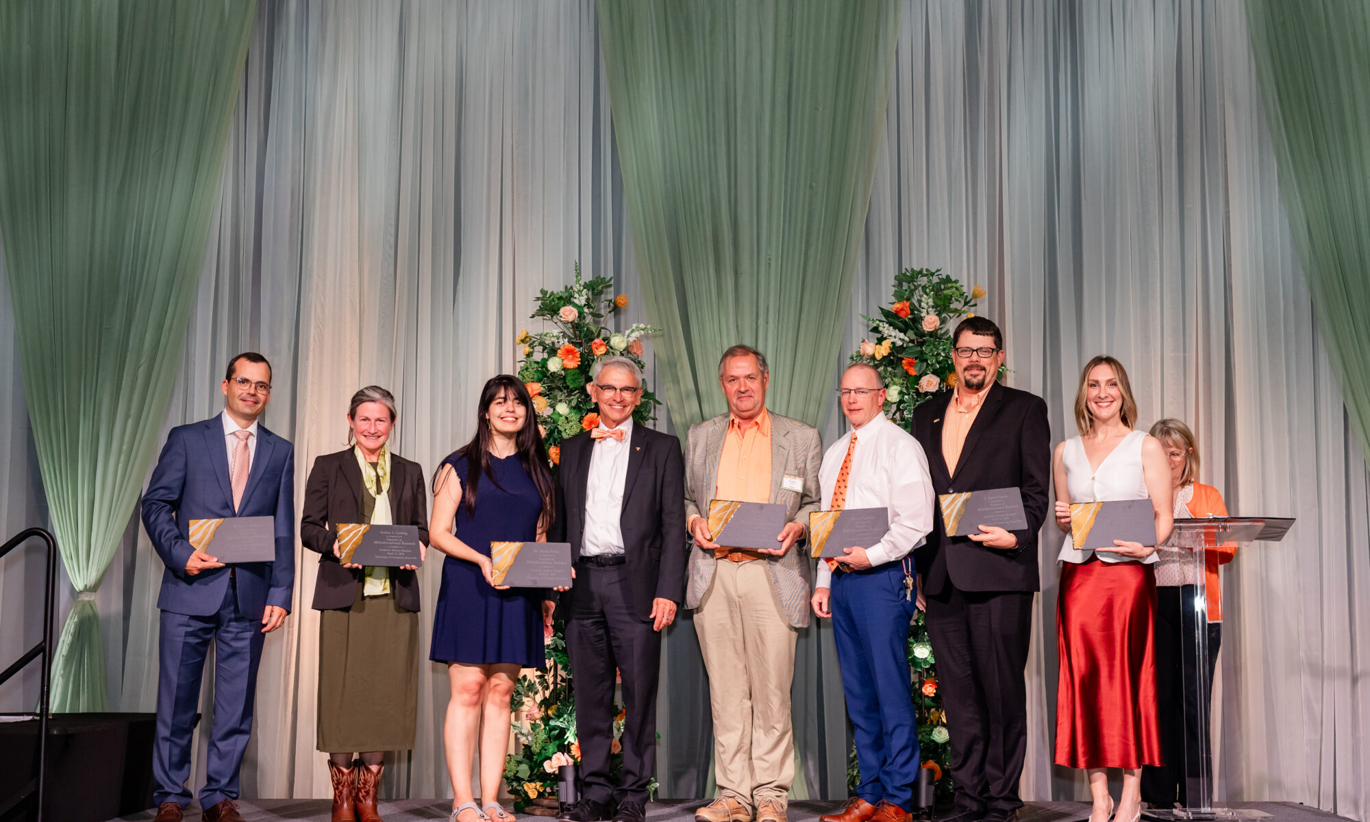 Photo of people standing on a stage with awards smiling