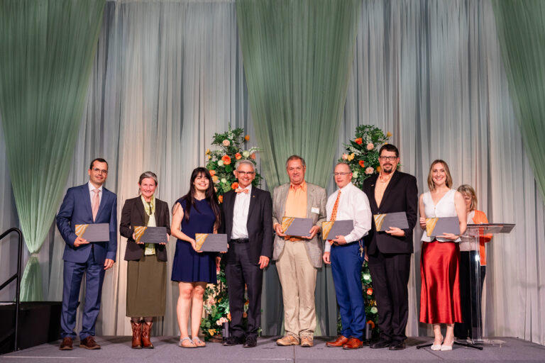 Photo of people standing on a stage with awards smiling