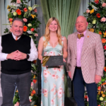 Photo of woman holding an award standing in between two men posing