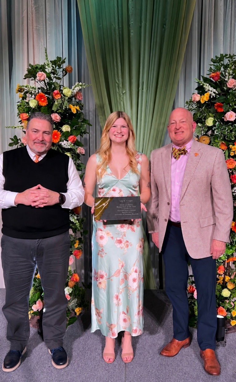 Photo of woman holding an award standing in between two men posing