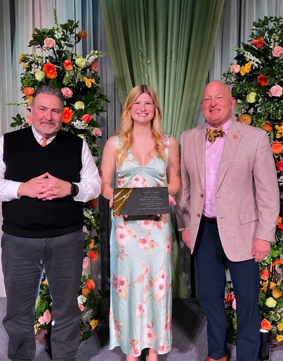 Photo of woman holding an award standing in between two men posing