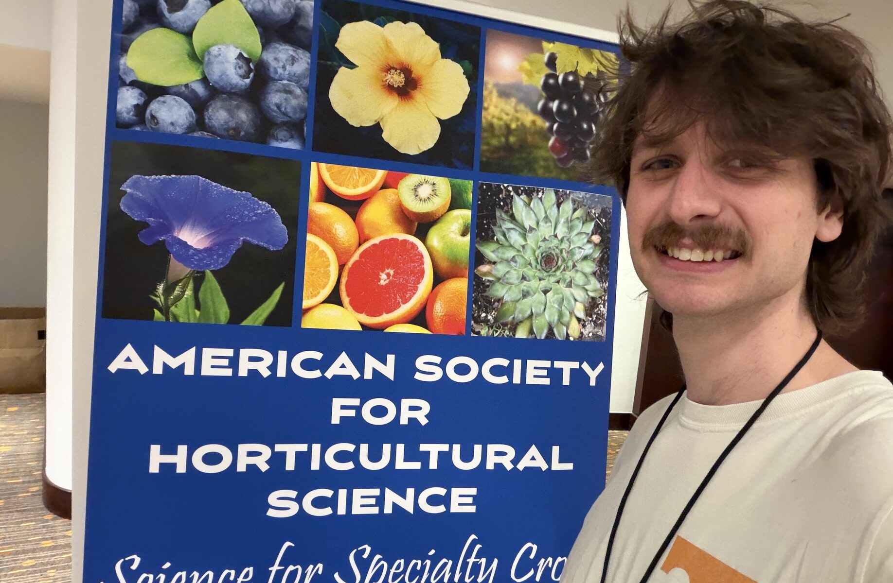 Photo of a man standing next to an American Society for Horticultural Science poster smiling