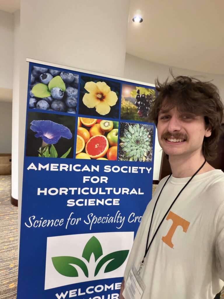 Photo of a man standing next to an American Society for Horticultural Science poster smiling