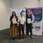 Three people standing in front of pull up banners holding awards