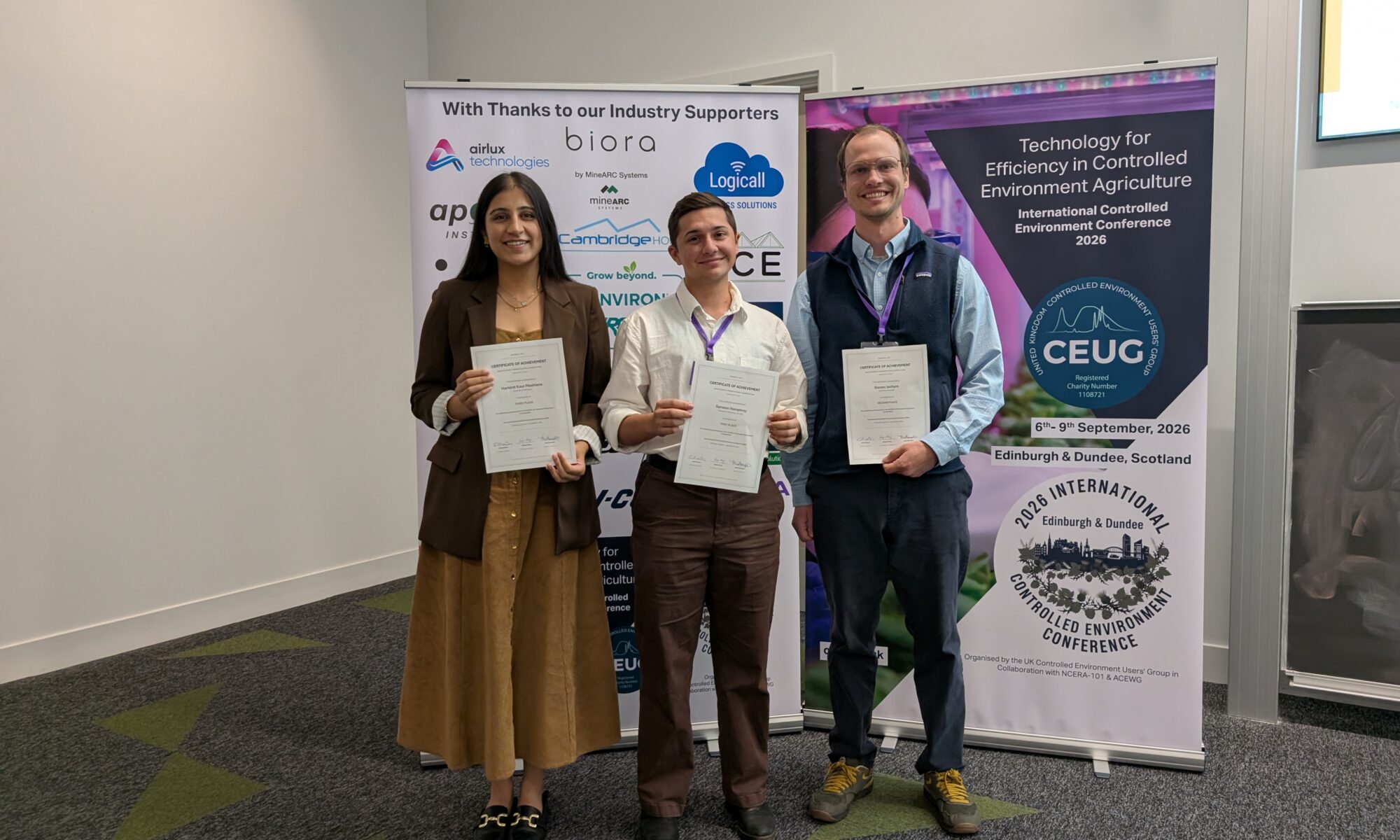 Three people standing in front of pull up banners holding awards