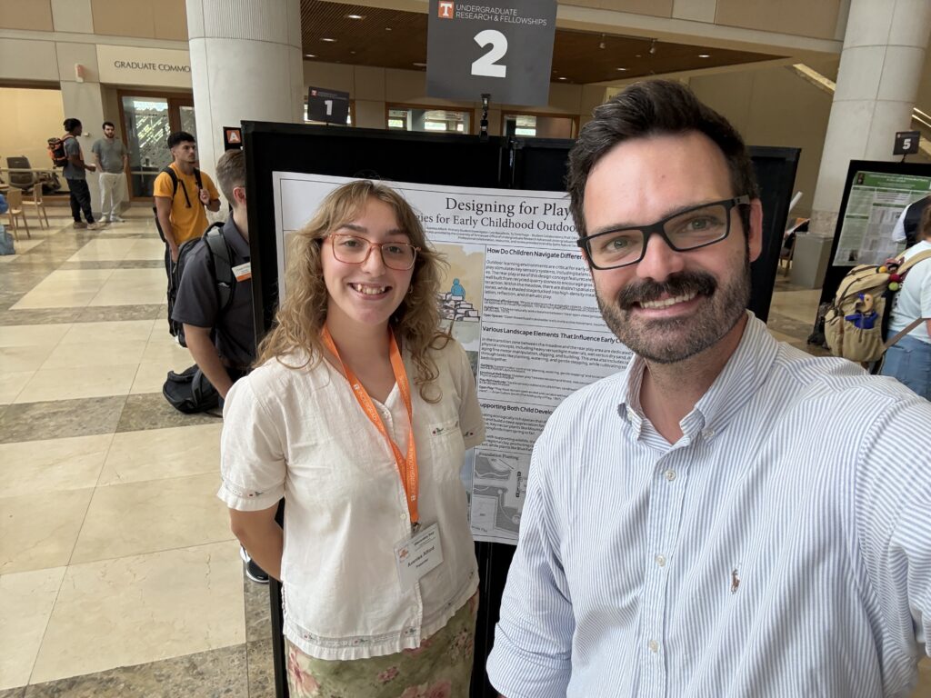 Woman and man smiling in front of a poster taking a selfie