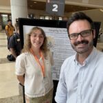 Woman and man smiling in front of a poster taking a selfie