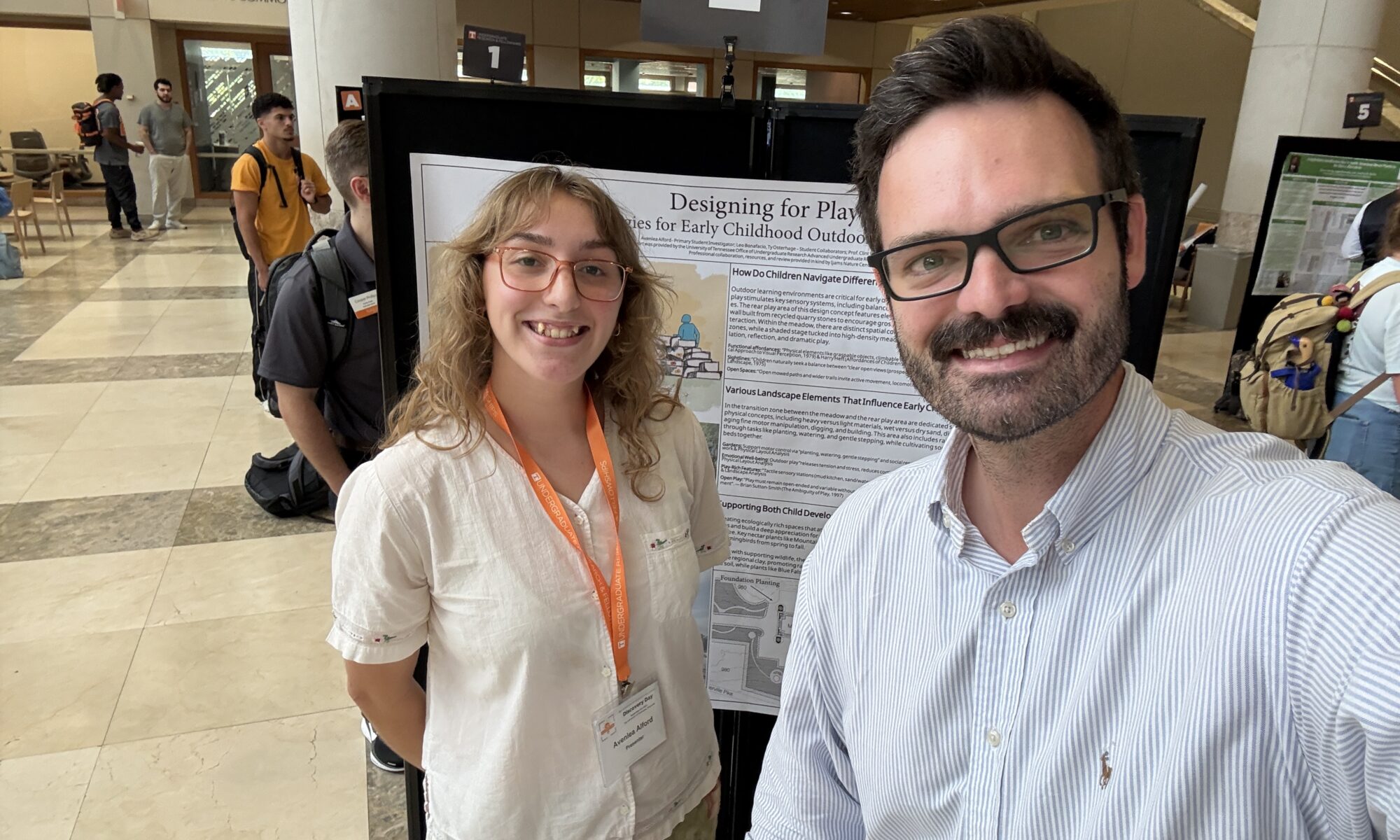 Woman and man smiling in front of a poster taking a selfie
