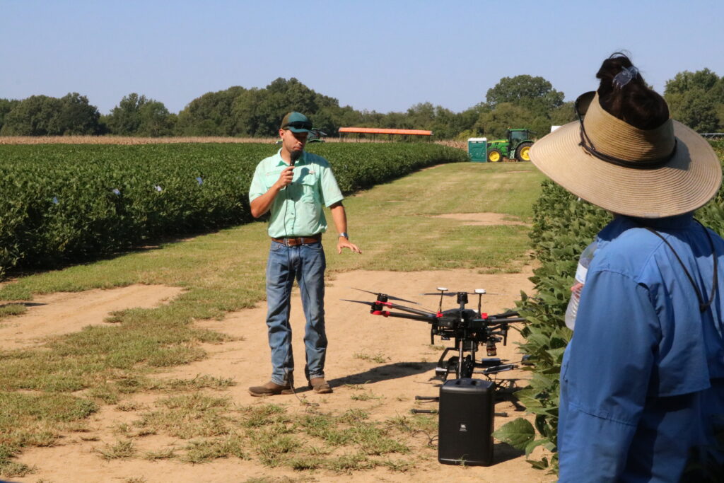 Man explaining a farming tool with a person listening on the side